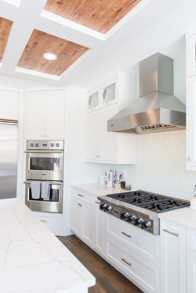 Brightly lit renovated kitchen featuring new stainless steel stove, hood, and oven set in custom white cabinetry.