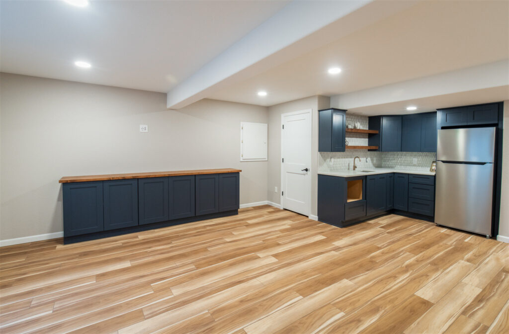 Open finished basement space in an Aurora, CO home is complete with new flooring, cabinetry, and a modern kitchenette.