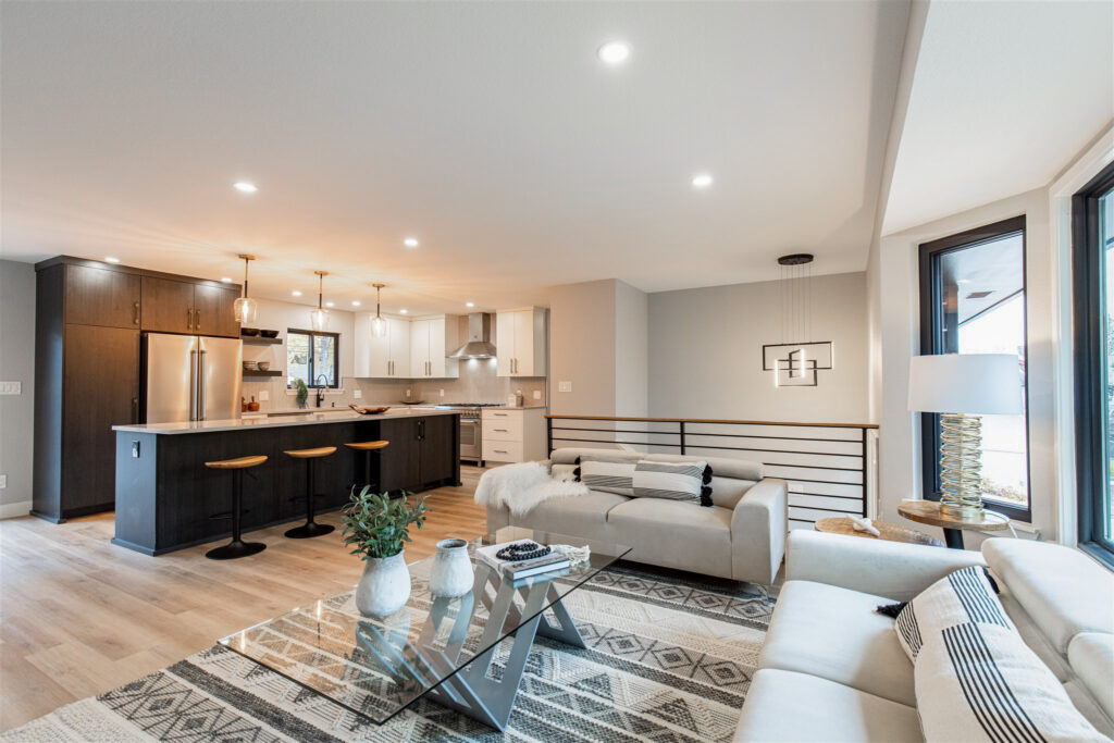 The view from a warmly-lit, renovated Boulder, CO living room shows a modern kitchen complete with new appliances and island with barstools.