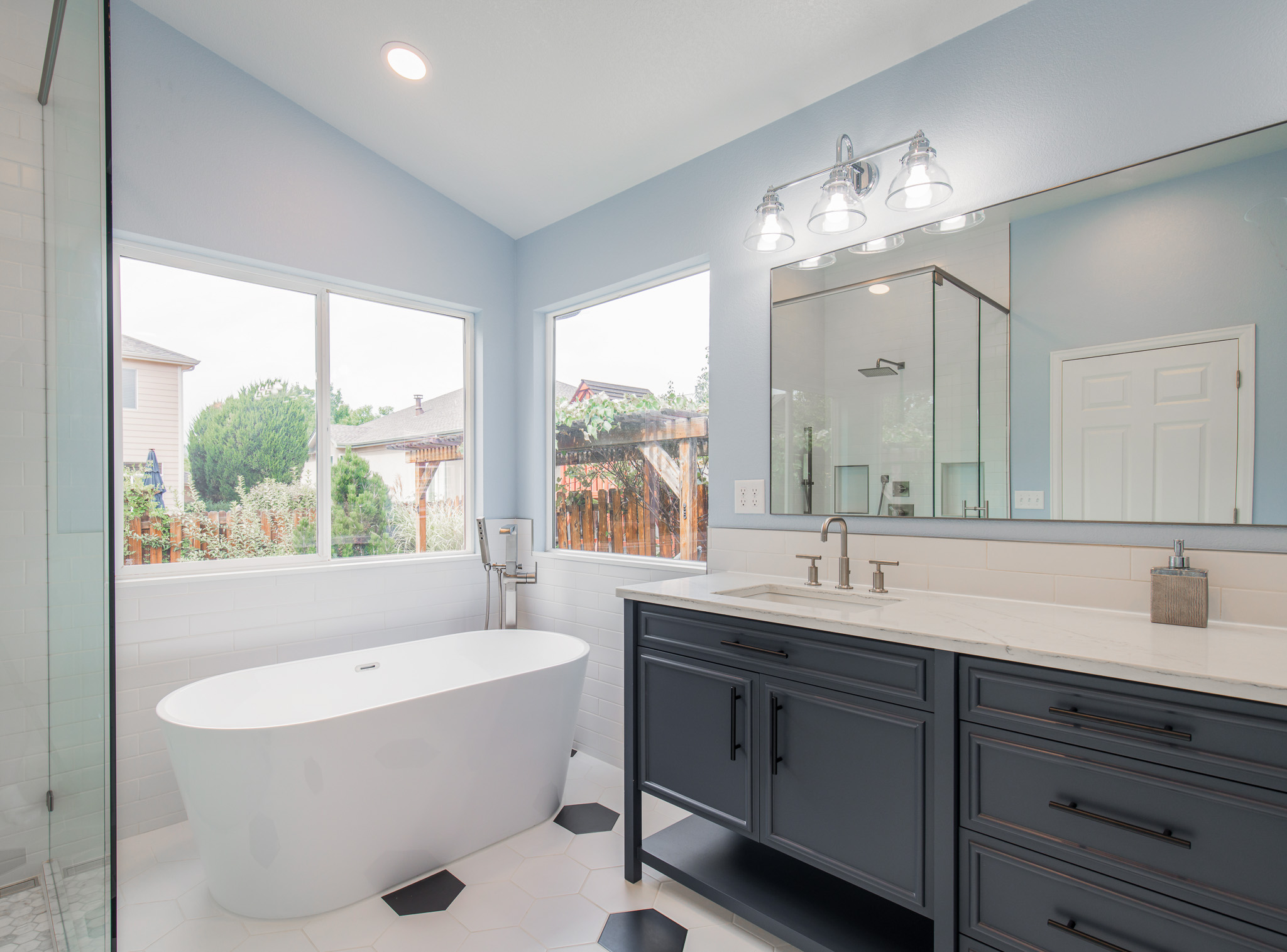 In the corner of a newly remodeled bathroom stands a white bathtub beneath a set of two windows.