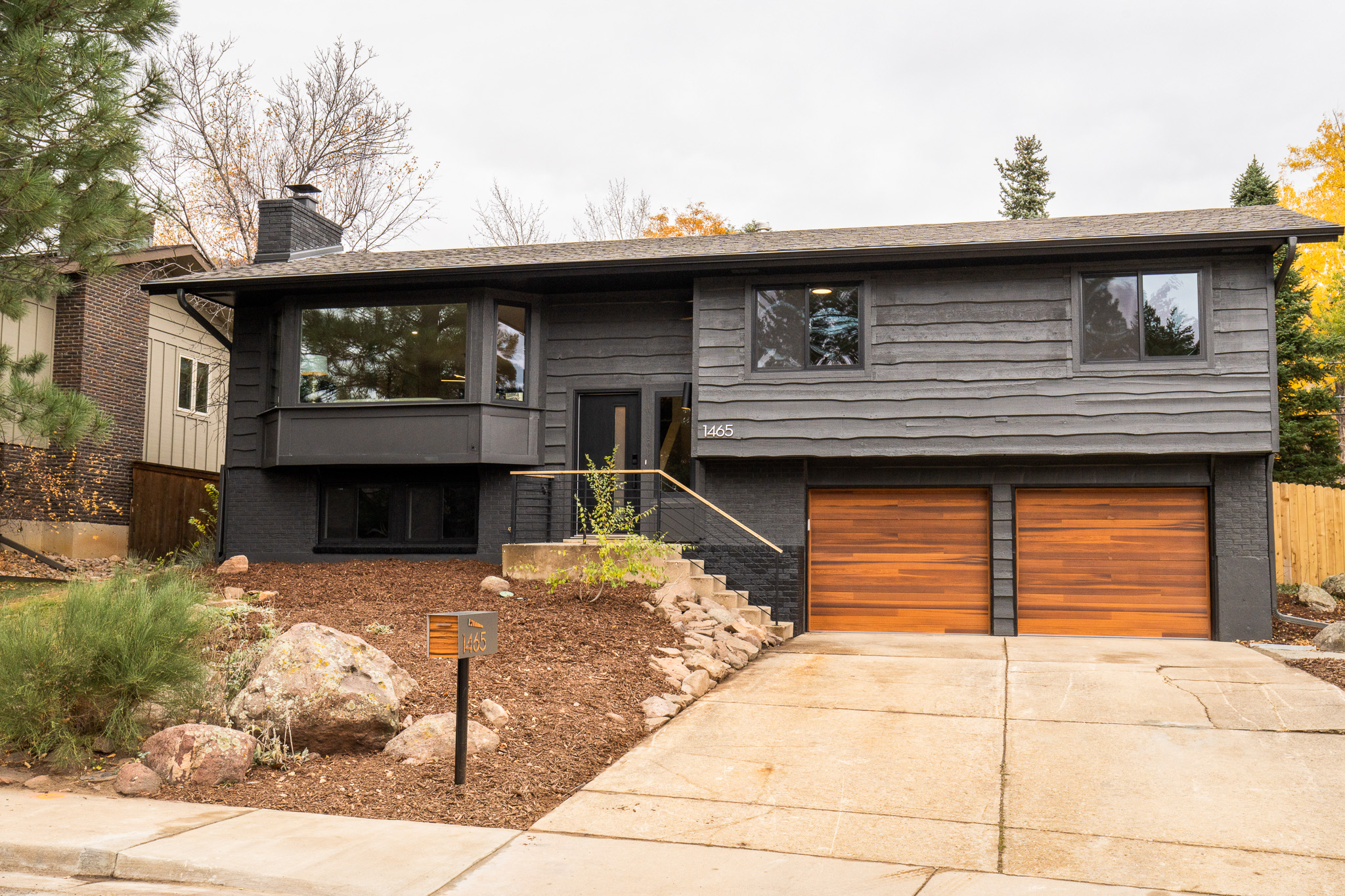 Exterior of a two-story home, featuring a new coat of black paint and two new cedar garage doors.
