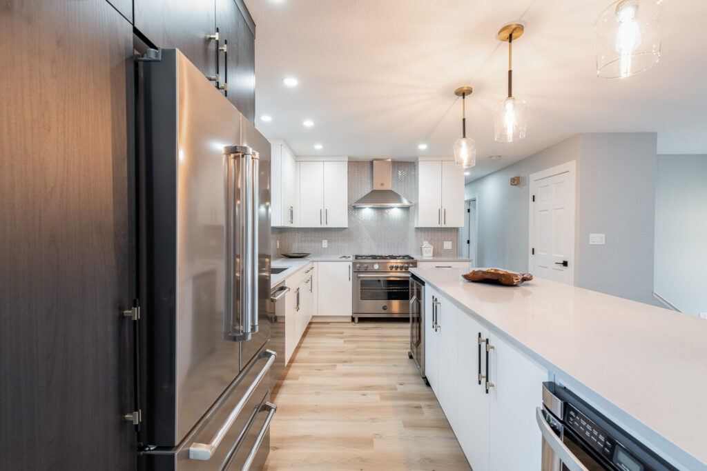 A new stainless steel oven, stove, and hood rest against the far wall of a newly renovated kitchen. In the foreground, a custom kitchen island with a dishwasher, wine holder, and custom cabinetry.