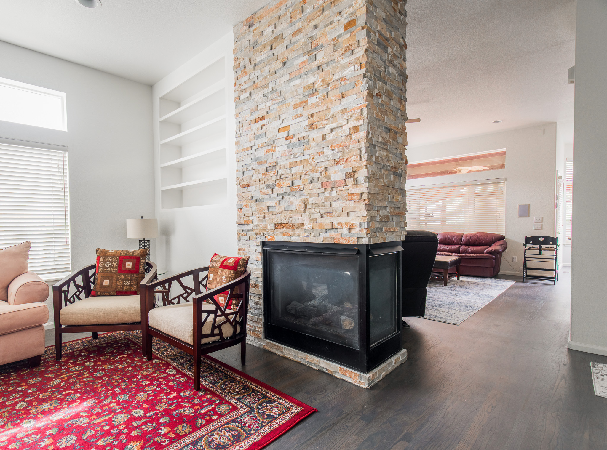A rustic brick fireplace stands at the center of newly constructed living room complete with furniture and bright red rug.