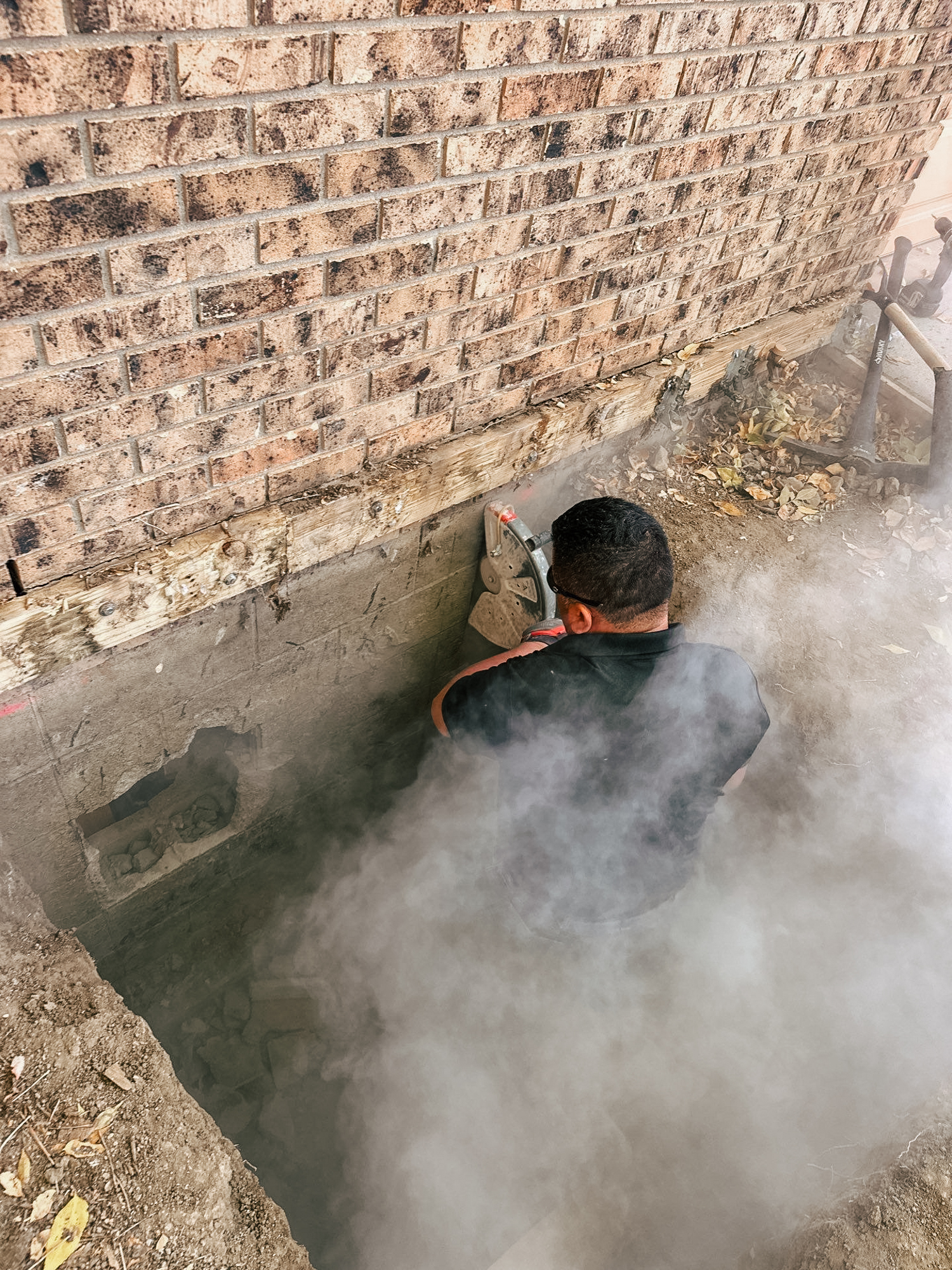 A crawl space access point is cut into the side of a house using a hand saw.